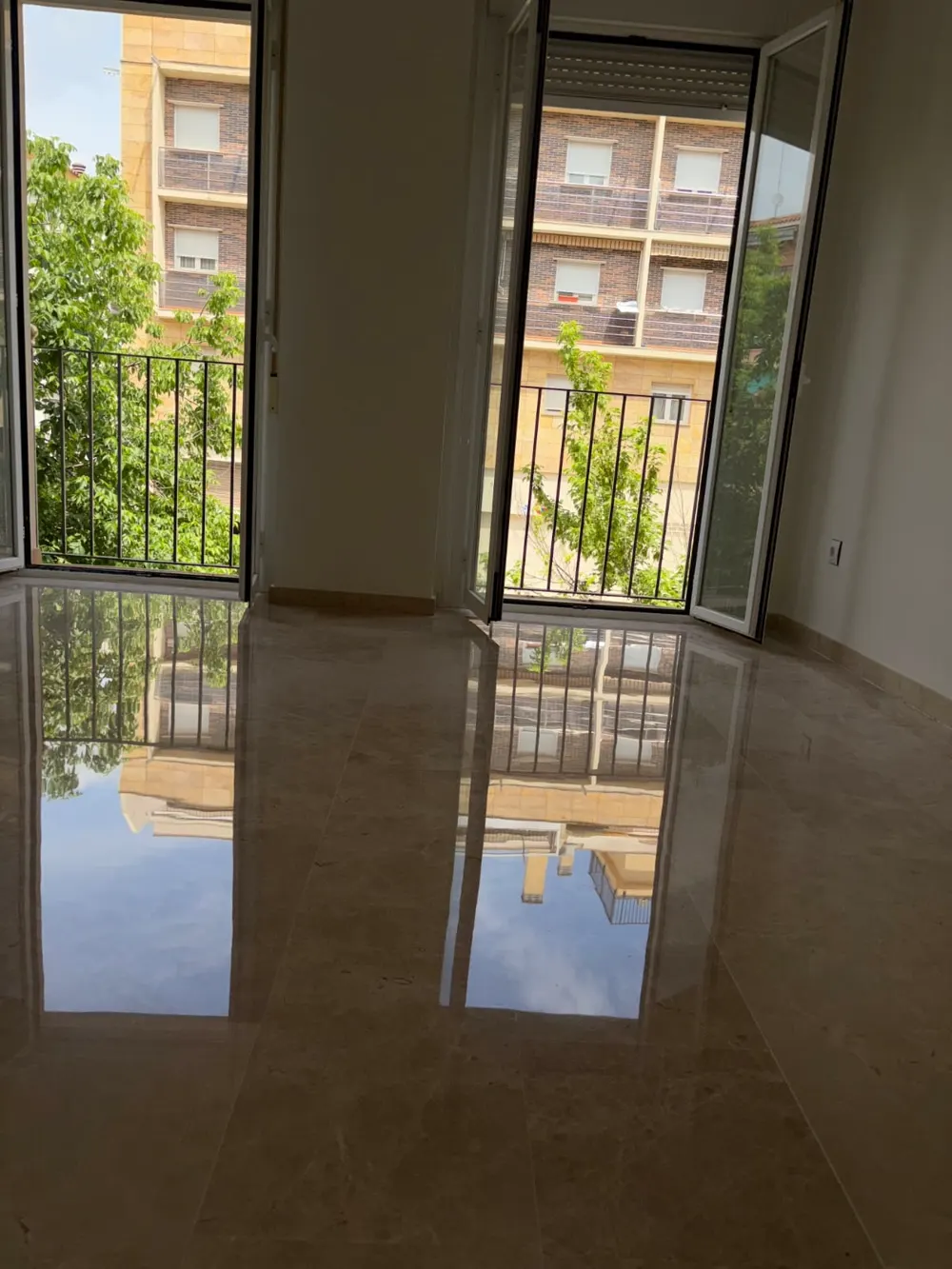 Mármol beige brillo espejo reflejando balcones y edificios — trabajo real de Pulimentos Jiménez