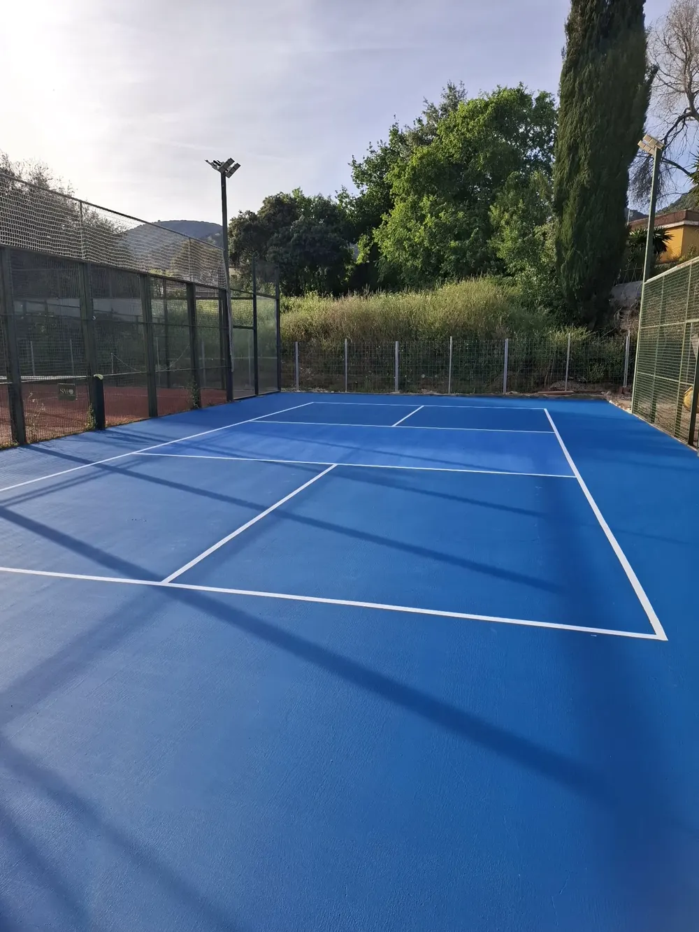 Pista deportiva azul terminada, vista general con vegetación — trabajo real de Pulimentos Jiménez