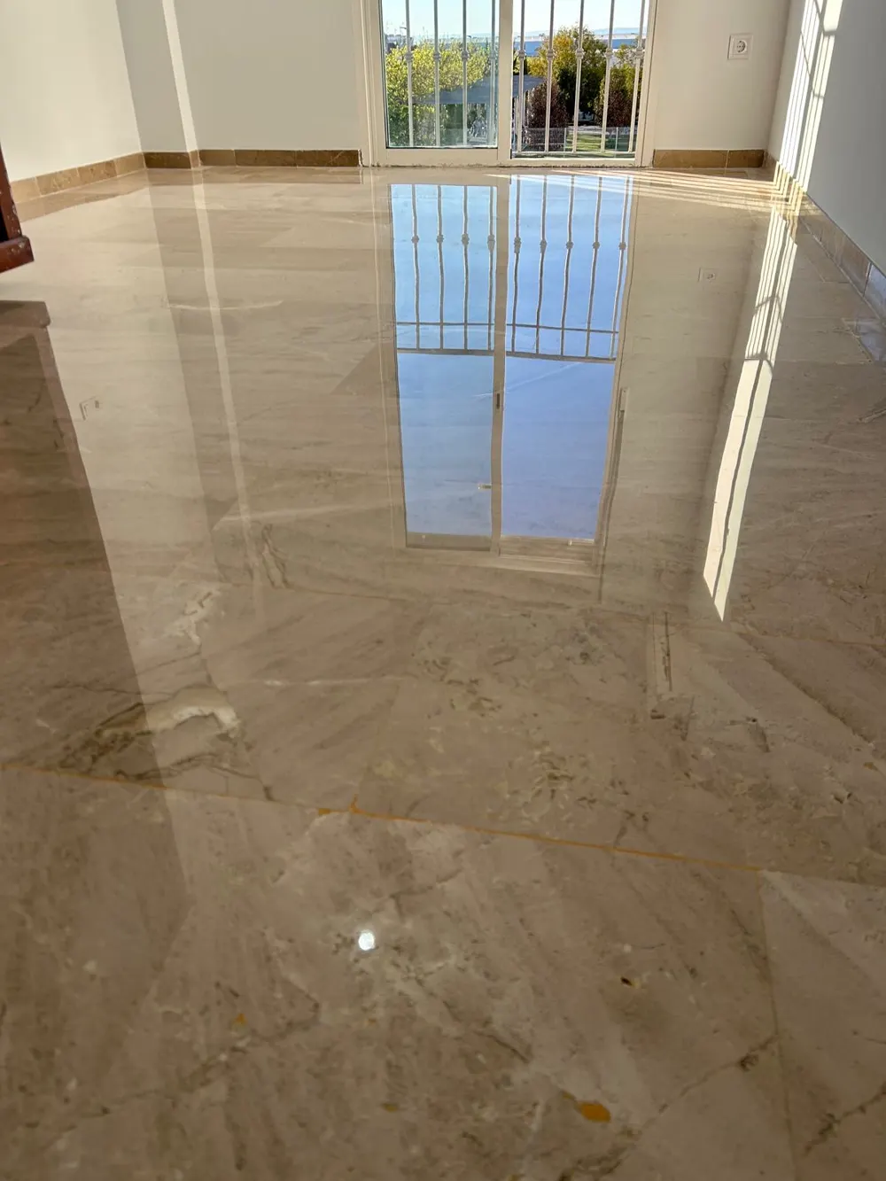 Mármol beige pulido con sol reflejando ventanal y reja — trabajo real de Pulimentos Jiménez