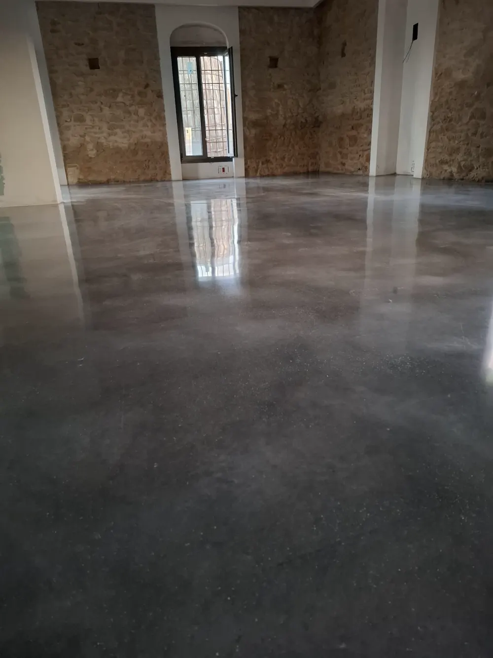 Hormigón pulido brillante en salón con muros de piedra — trabajo real de Pulimentos Jiménez