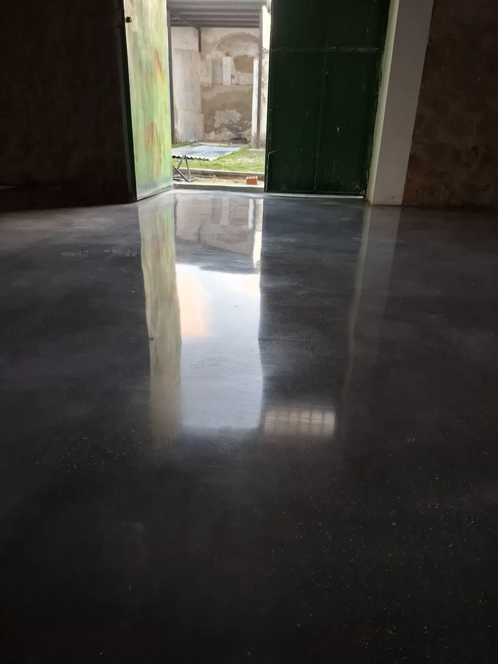 Nave con hormigón oscuro pulido espejo, portón verde antiguo — trabajo real de Pulimentos Jiménez