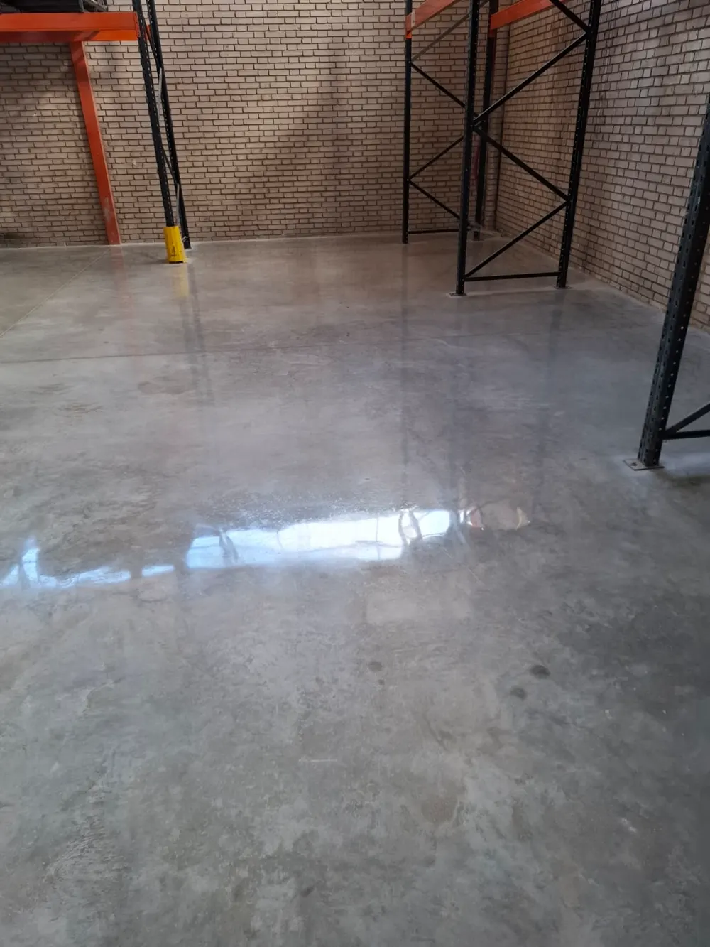 Hormigón pulido en nave de ladrillo con estanterías naranjas — trabajo real de Pulimentos Jiménez