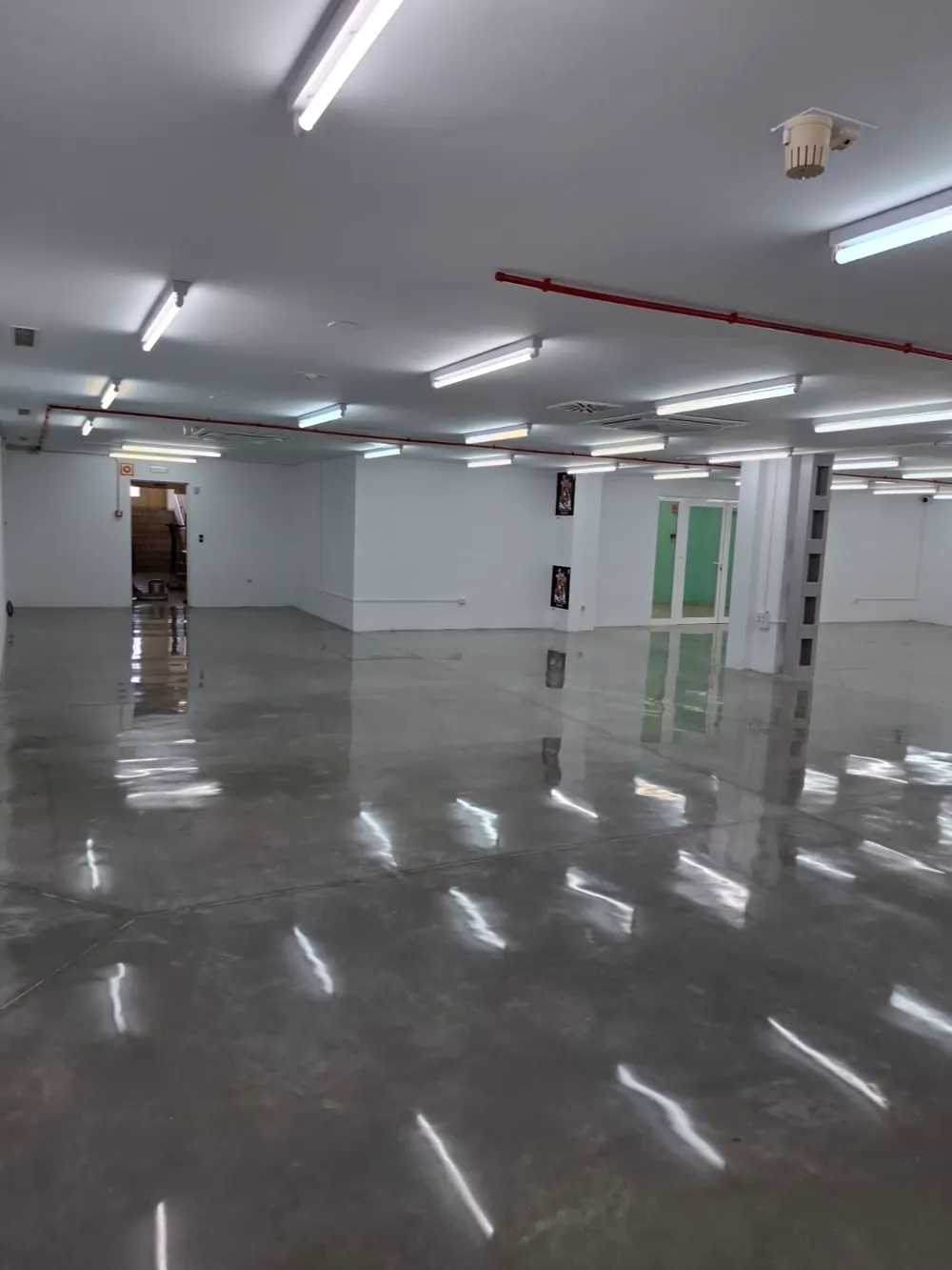 Local comercial amplio con cemento pulido y fluorescentes reflejados — trabajo real de Pulimentos Jiménez
