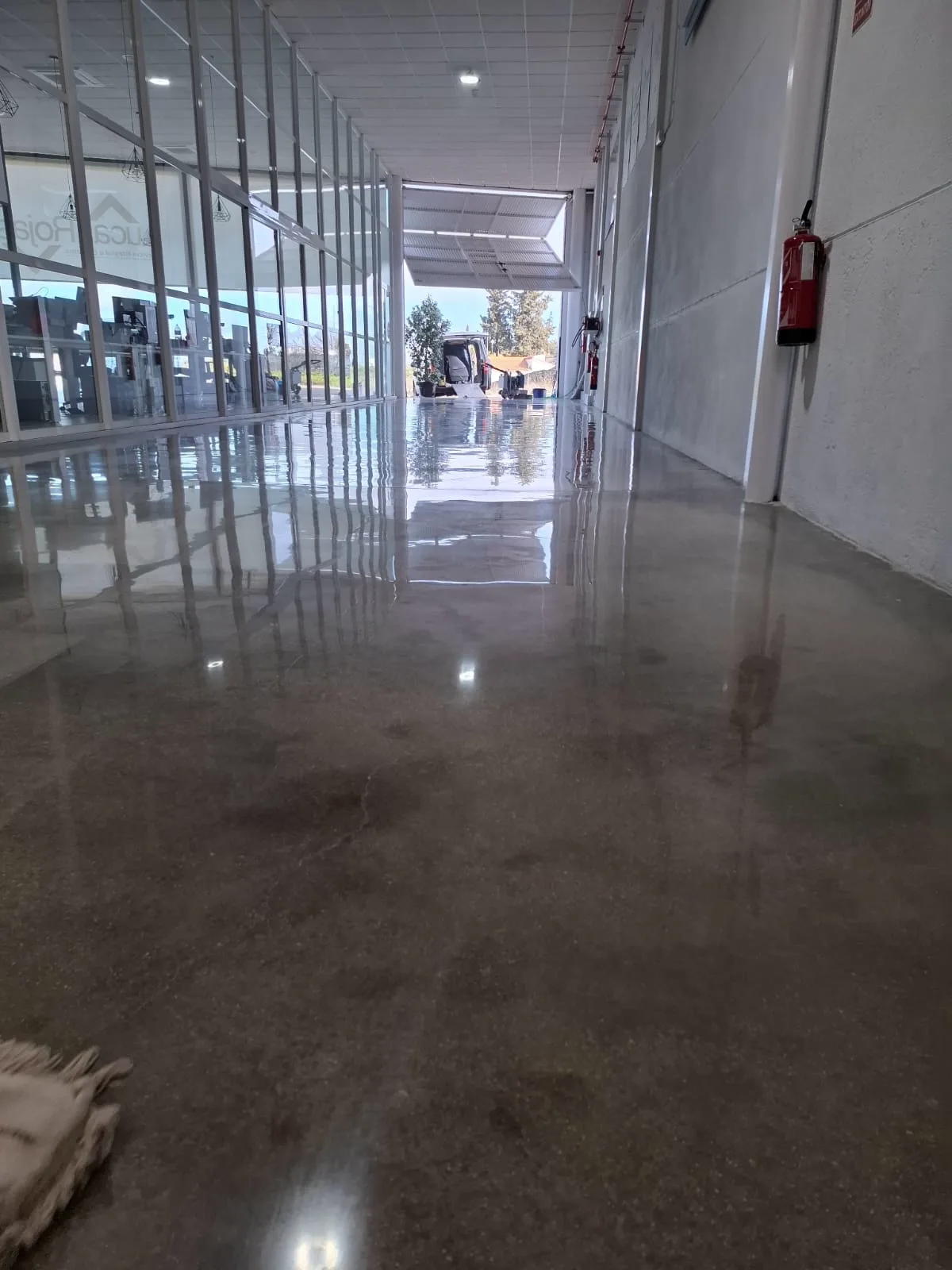 Pasillo de nave con hormigón pulido a espejo que refleja la cristalera — trabajo real de Pulimentos Jiménez