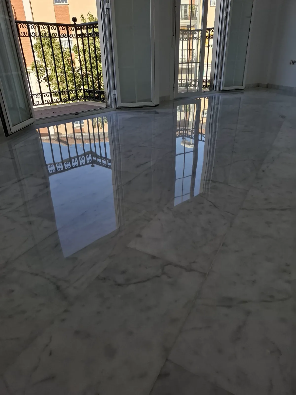 Mármol blanco pulido con brillo espejo reflejando los balcones — trabajo real de Pulimentos Jiménez