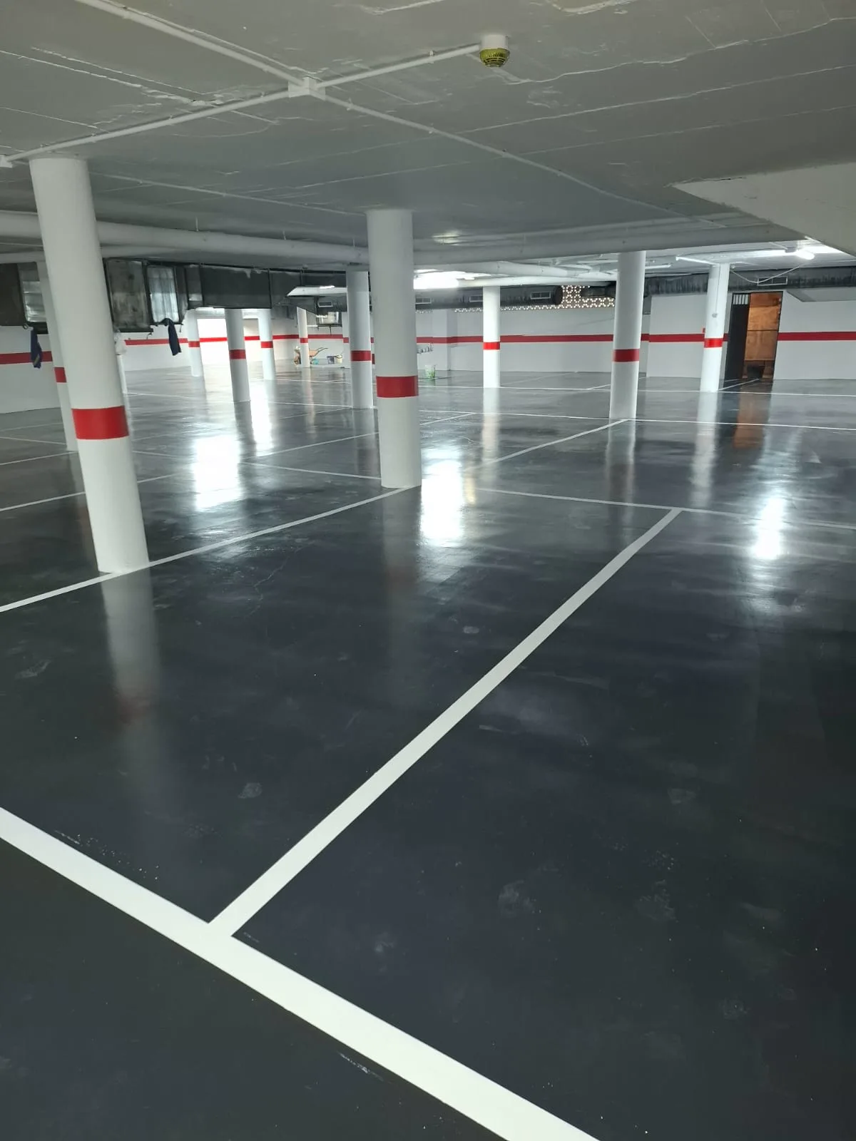 Parking pintado en gris con plazas y líneas blancas recién marcadas — trabajo real de Pulimentos Jiménez